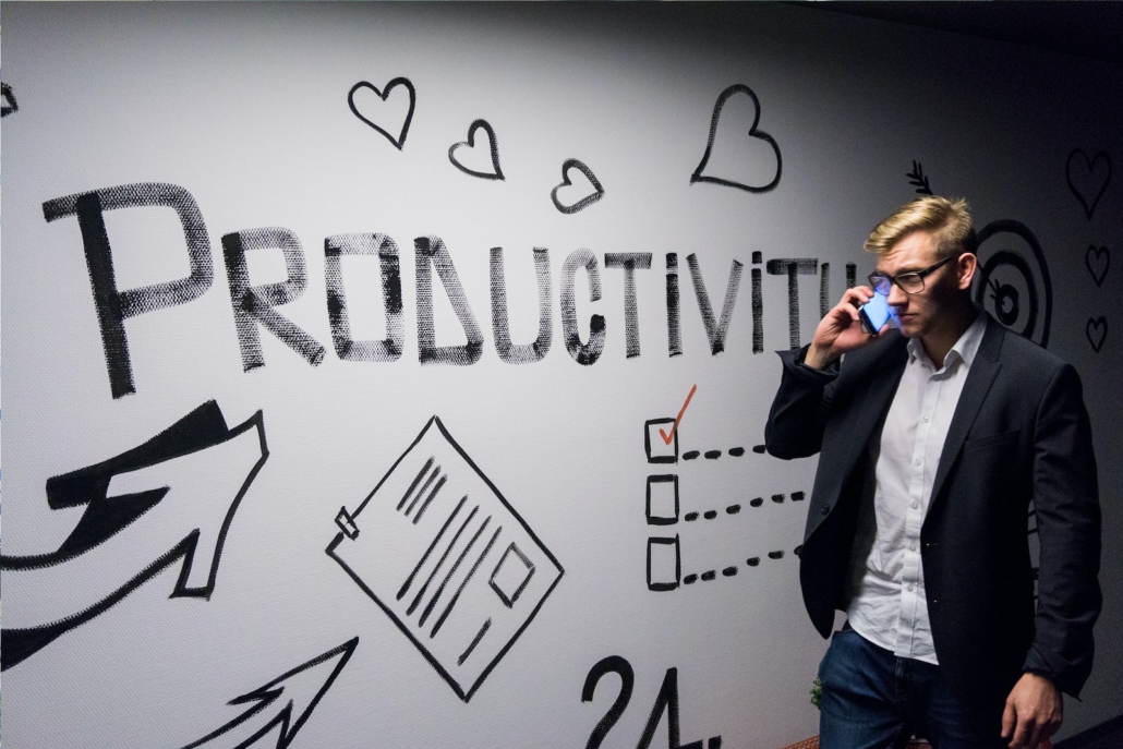 Productivity Hacks - Man holding smartphone looking at productivity wall decor